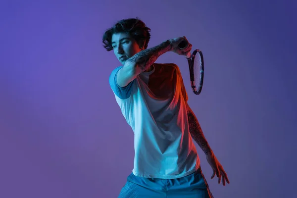 Ung kaukasier man spelar tennis isolerad på lila-blå studio bakgrund i neon, action och motion koncept — Stockfoto