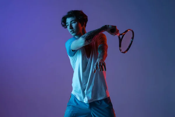 Joven hombre caucásico jugando al tenis aislado en el fondo del estudio púrpura-azul en neón, acción y concepto de movimiento —  Fotos de Stock