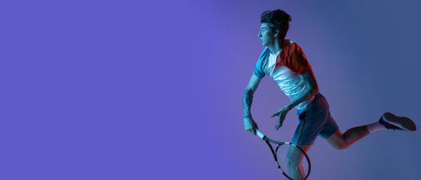 Joven hombre caucásico jugando al tenis aislado en el fondo del estudio púrpura-azul en neón, acción y concepto de movimiento —  Fotos de Stock