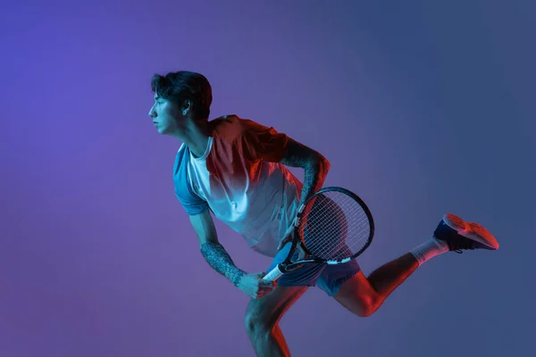 Молодий кавказький чоловік грає в теніс ізольований на фіолетово-блакитному студійному фоні в неоні, дії і концепції руху — стокове фото