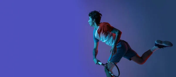 Ung kaukasier man spelar tennis isolerad på lila-blå studio bakgrund i neon, action och motion koncept — Stockfoto