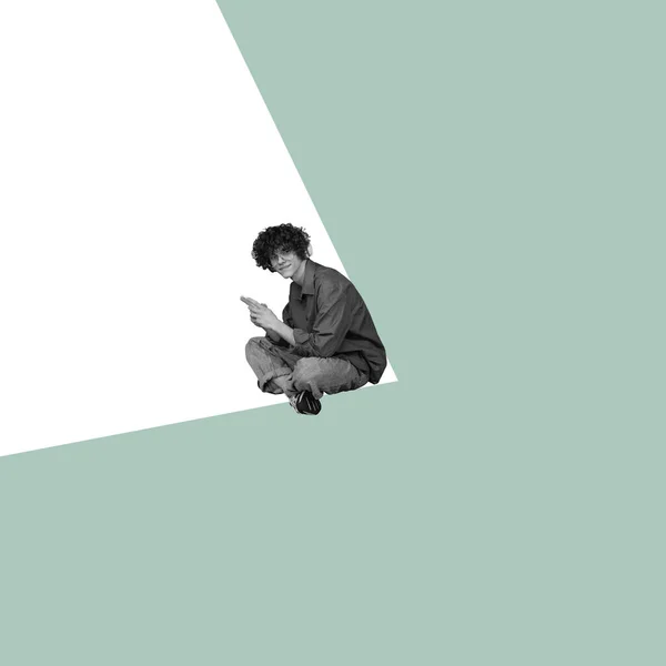 Moderní design, koláž současného umění. Inspirace, nápad, módní styl městského časopisu. Mladý muž sedí v bílém úhlu na pastelové zelené pozadí — Stock fotografie
