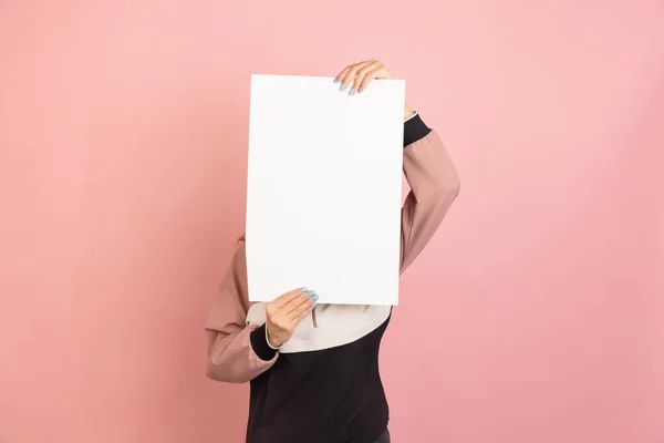 Una mujer joven con una hoja de papel vacía con espacio de copia para anuncios aislados en el fondo del estudio rosa. — Foto de Stock