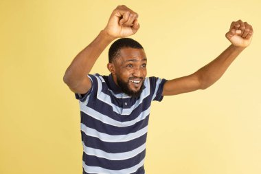 Bir Afrikalı genç, sarı stüdyo arka planında izole edilmiş bir şekilde poz veriyor.