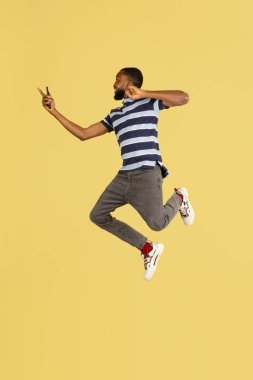 Bir Afrikalı genç, sarı stüdyo arkaplanının üzerinden atlıyor. Reklam için kopyalama alanı var.