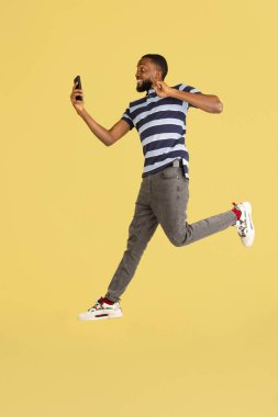 Bir Afrikalı genç, sarı stüdyo arkaplanının üzerinden atlıyor. Reklam için kopyalama alanı var.