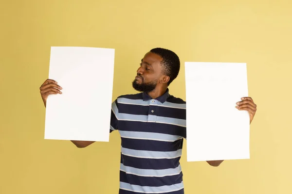 Happy African man with blank sheets of paper isolated over yellow studio background