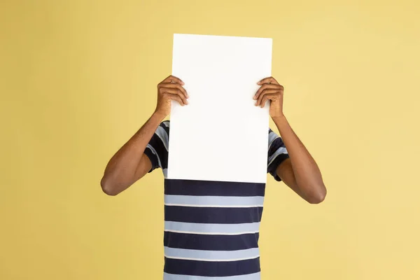Happy African man with blank sheet of paper isolated over yellow studio background — Stock Photo, Image