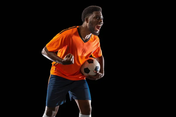 Портрет молодого африканського футболіста, який зображає себе ізольованим на чорному тлі. Концепція спорту. — стокове фото