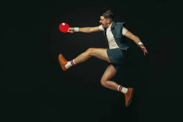 Молодий кавказький чоловік грає в теніс ізольовано на чорному студійному фоні в ретро-стилі, дії і концепції руху — стокове фото