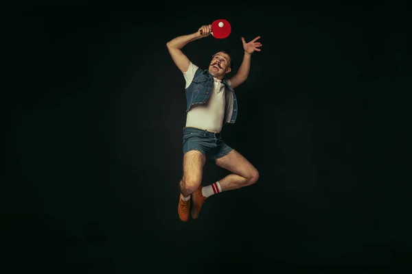 Jovem caucasiano jogando tênis isolado no fundo do estúdio preto em estilo retro, ação e conceito de movimento — Fotografia de Stock