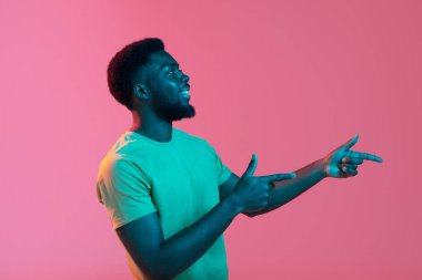 Neon rengi pembe stüdyo arka planında Afrikalı genç adam portresi. İnsan duyguları kavramı, yüz ifadesi, gençlik, satış, reklam.