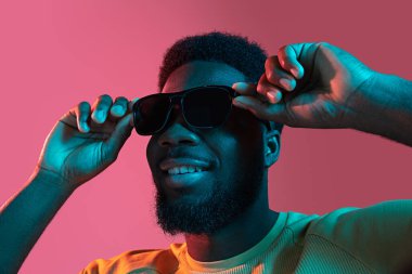 Neon rengi pembe stüdyo arka planında Afrikalı genç adam portresi. İnsan duyguları kavramı, yüz ifadesi, gençlik, satış, reklam.