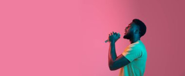 Neon rengi pembe stüdyo arka planında Afrikalı genç adam portresi. İnsan duyguları kavramı, yüz ifadesi, gençlik, satış, reklam.