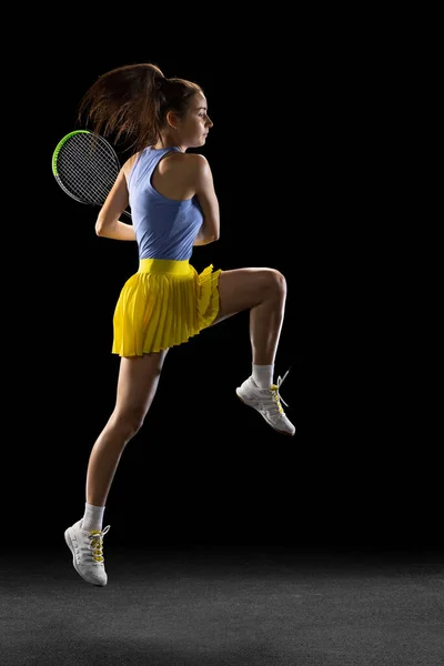 Jeune femme caucasienne jouant au tennis isolé sur fond de studio noir en action et mouvement, concept sportif — Photo