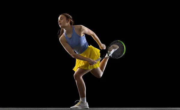 Jovem caucasiana jogando tênis isolado no fundo do estúdio preto em ação e movimento, conceito de esporte — Fotografia de Stock
