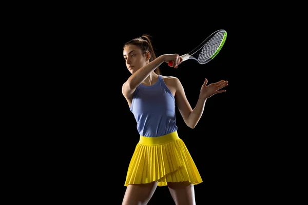 Молода біла жінка грає в теніс ізольовано на чорному студійному фоні в дії і русі, спортивна концепція — стокове фото