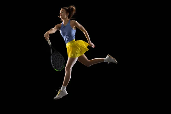 Jeune femme caucasienne jouant au tennis isolé sur fond de studio noir en action et mouvement, concept sportif — Photo