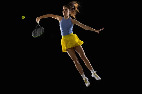 Giovane donna caucasica che gioca a tennis isolato su sfondo nero studio in azione e movimento, concetto di sport — Foto Stock