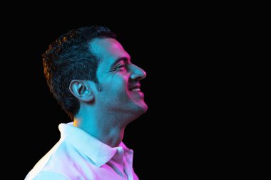 Latina 'nın Neon' daki karanlık stüdyo arka planında genç adam portresi. İnsan duyguları kavramı, yüz ifadesi, gençlik, satış, reklam.