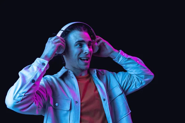 Retrato de hombre joven caucásico sobre fondo de estudio oscuro en neón. Concepto de emociones humanas, expresión facial. — Foto de Stock