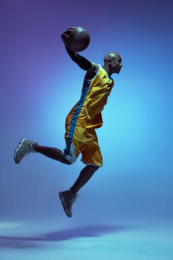 Handsome african-american male basketball player in action and motion in neon light on blue background. Concept of healthy lifestyle, professional sport.