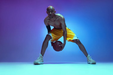 Close-up sportive athletic african-american male basketball player posing in neon light on blue background.
