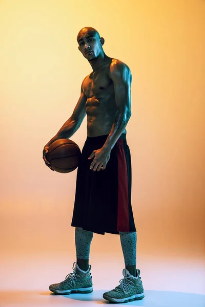 Sportive muscular african-american male basketball player posing in neon light on orange background. — Foto de Stock