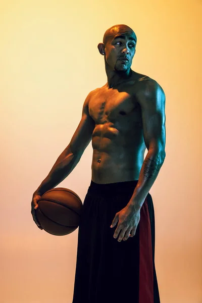 Sportive muscular african-american male basketball player posing in neon light on orange background. — Zdjęcie stockowe