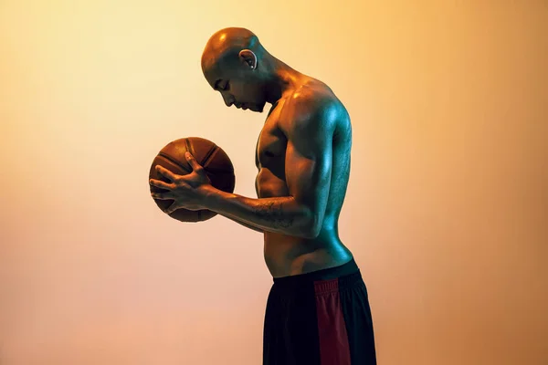 Handsome african-american male basketball player posing in neon light on orange background. — Zdjęcie stockowe