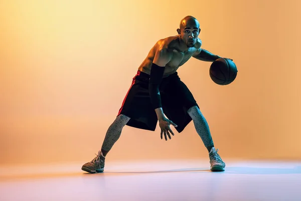 Portrait of african-american professional male basketball player in action in neon light on orange background. — Zdjęcie stockowe