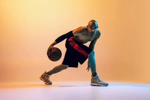 Portrait of african-american professional male basketball player in action in neon light on orange background. — 图库照片