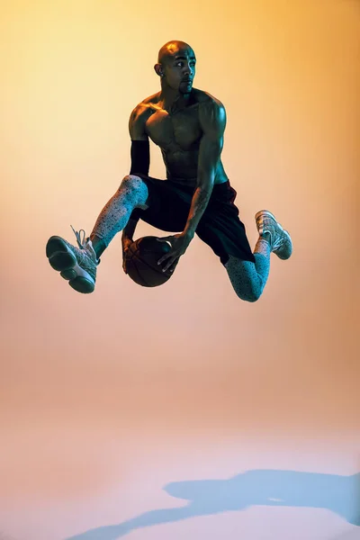 Портрет афроамериканського професійного баскетболіста в дії на неоновому світлі на помаранчевому фоні . — стокове фото