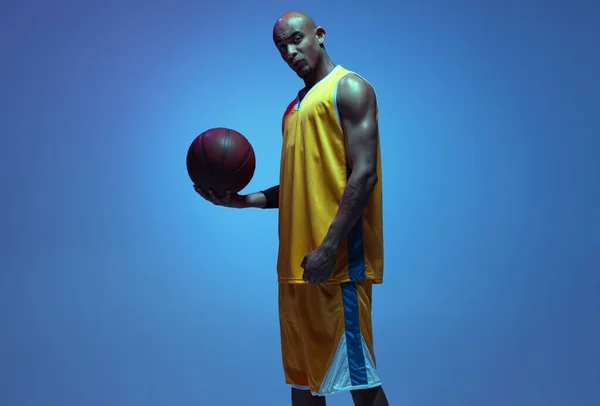 Sportive athletic african-american male basketball player posing in neon light on blue background. — Zdjęcie stockowe