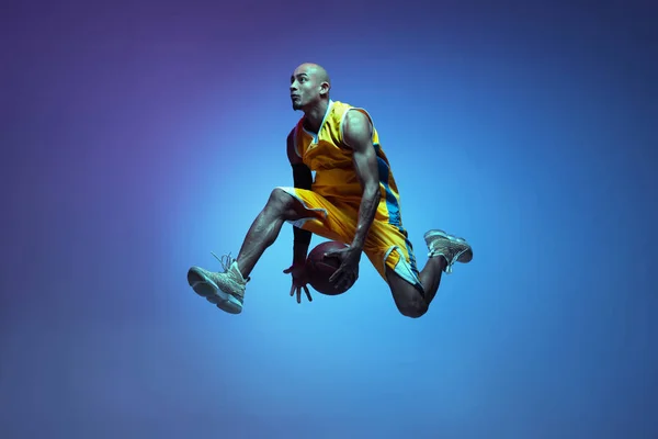 Sportive athletic african-american male basketball player training in neon light on blue background. — Fotografia de Stock