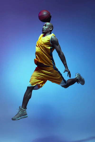 Handsome african-american male basketball player in action and motion in neon light on blue background. Concept of healthy lifestyle, professional sport. — Zdjęcie stockowe