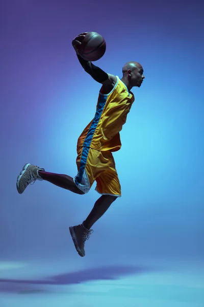 Handsome african-american male basketball player in action and motion in neon light on blue background. Concept of healthy lifestyle, professional sport. — Foto de Stock