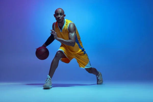 Sportive athletic african-american male basketball player training in neon light on blue background. — Foto de Stock