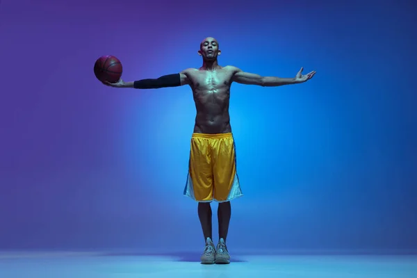 Sportive athletic african-american male basketball player posing in neon light on blue background. — Zdjęcie stockowe
