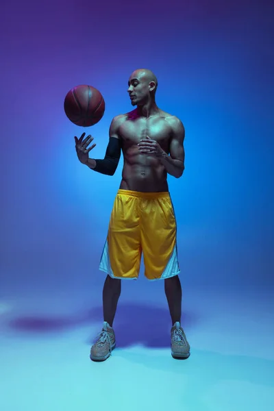 Handsome african-american male basketball player posing in neon light on blue background. Concept of healthy lifestyle, professional sport. — Stockfoto