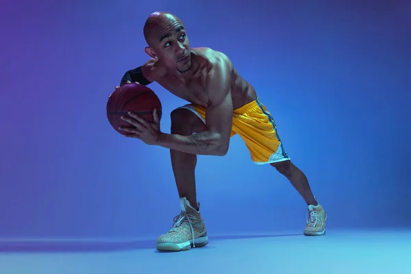 Close-up sportive athletic african-american male basketball player posing in neon light on blue background. — Fotografia de Stock