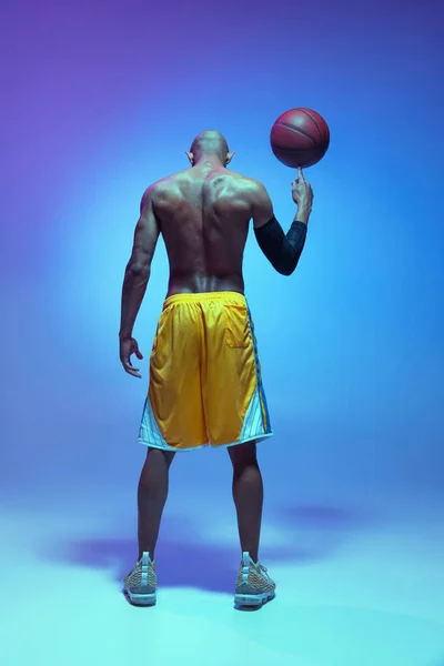 Sportive athletic african-american male basketball player posing in neon light on blue background. Rear view — Zdjęcie stockowe