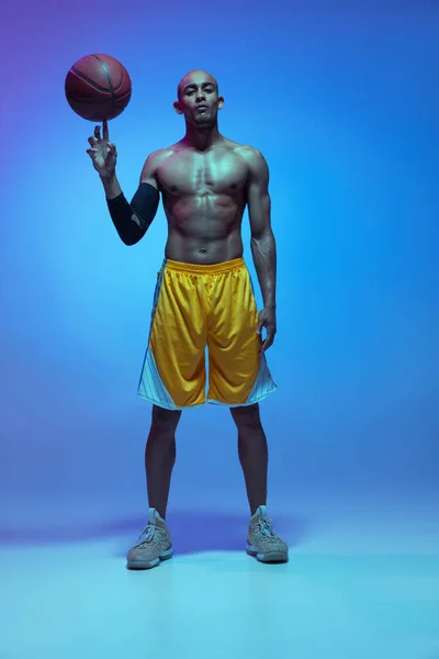 Sportive athletic african-american male basketball player posing in neon light on blue background. — Foto de Stock