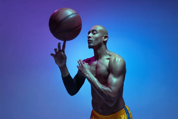 Strong muscular african-american male basketball player training in neon light on orange background. — Photo