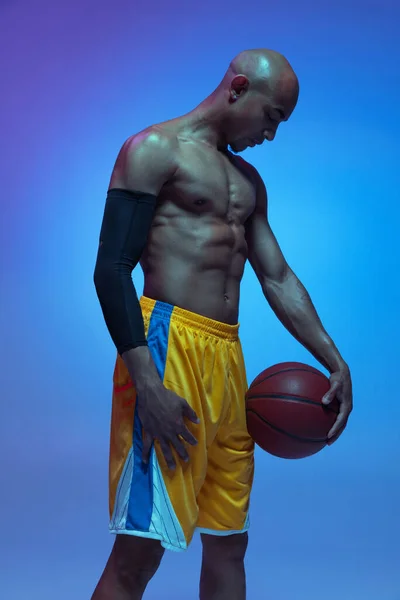 Handsome african-american male basketball player posing in neon light on blue background. Concept of healthy lifestyle, professional sport. — Stockfoto