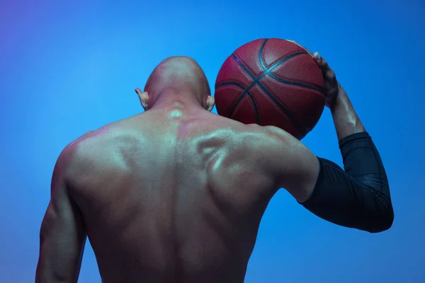 Close-up back view of athletic african-american male basketball player posing in neon light on blue background. — Zdjęcie stockowe