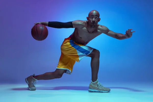 Sportive athletic african-american male basketball player training in neon light on blue background. — Zdjęcie stockowe