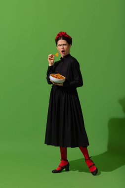 Young woman in art action remaking greatest paintings on green background. Retro style, comparison of eras concept.