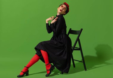 Young beautiful woman in image of famous painter, artist Frida Kahlo on green background.