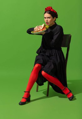 Young woman in art action remaking greatest paintings on green background. Retro style, comparison of eras concept.